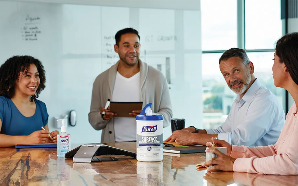 Group of coworkers in a conference room at a table with a conference phone and container of Purell wipes on top